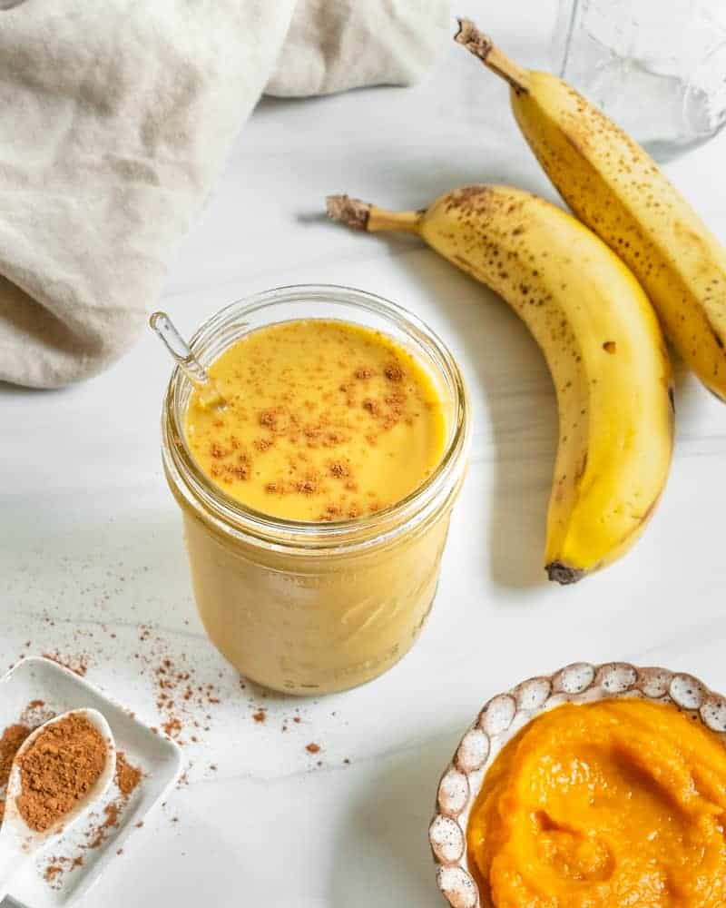 finished pumpkin pie smoothie in a glass jar with ingredients in the background