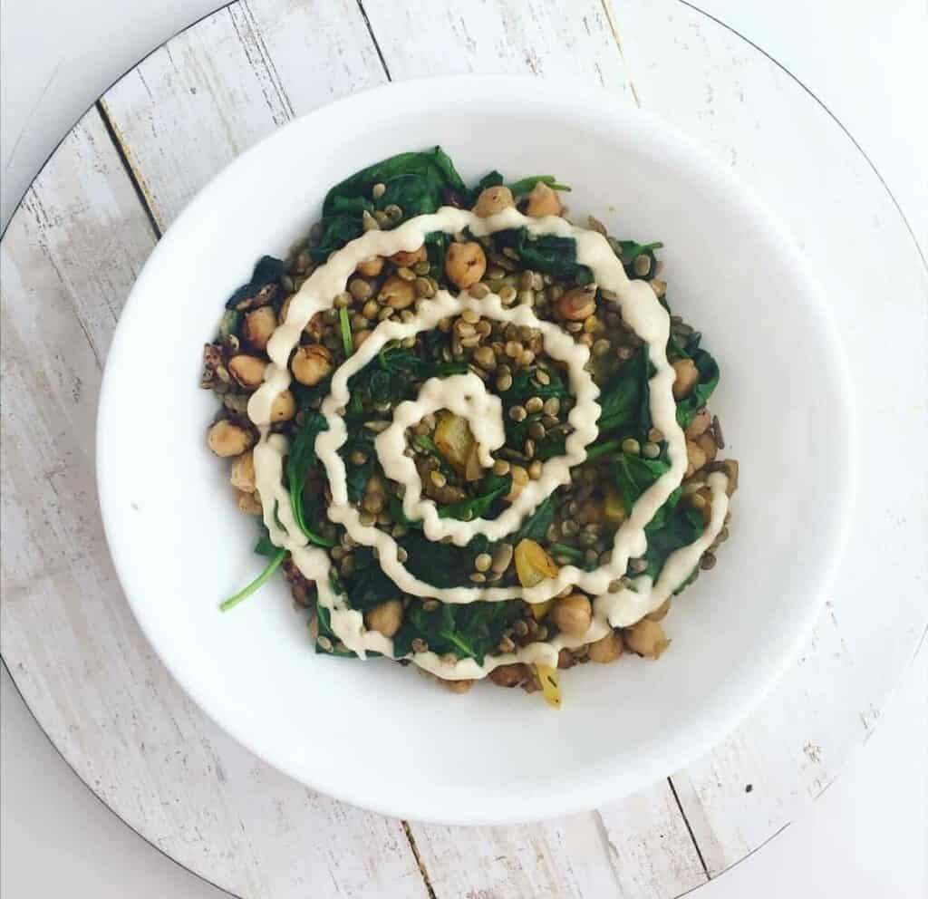 finished lentil chickpea salad in a bowl with dressing swirled on top against a white bacgkround
