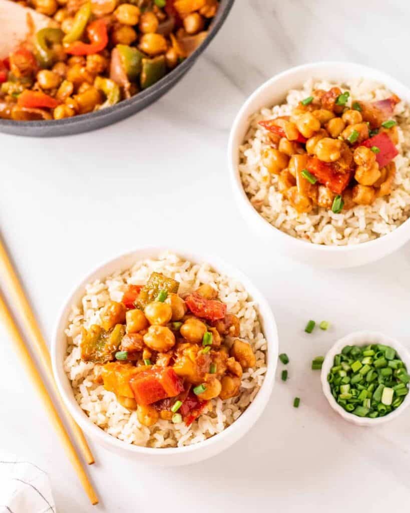 two completed bowls of sweet and sour chickpea dish against a white background with chopsticks on the side