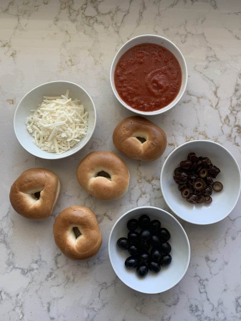 ingredients for halloween spider bagel bites measured out against a white marble surface