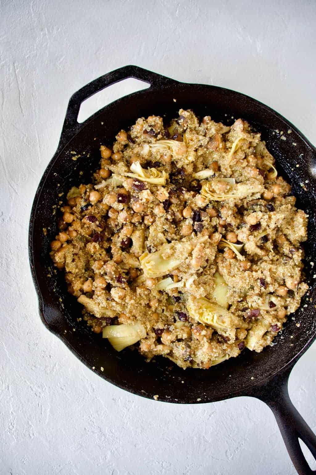 process of Artichoke Hearts Quinoa Salad being cooked in a cast iron skillet against white background