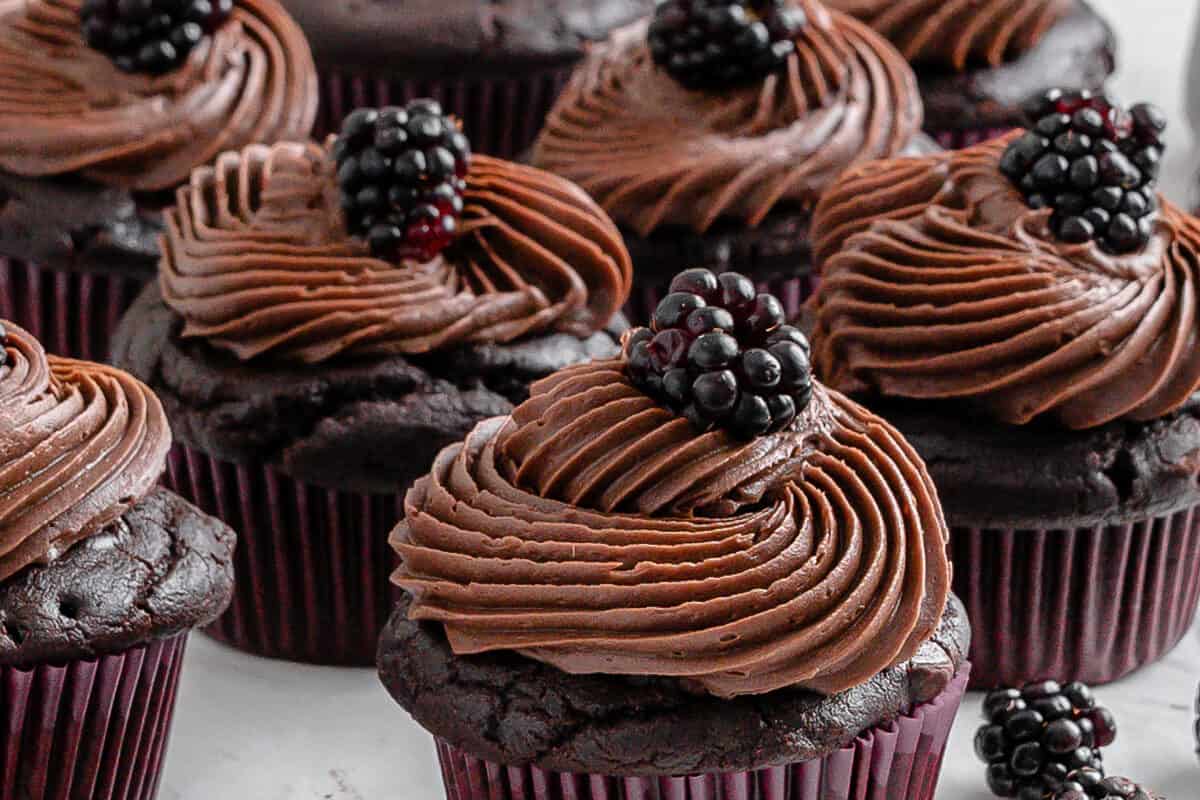 completed Blackberry Chocolate Cupcakes with blackberries scattered against a white surface