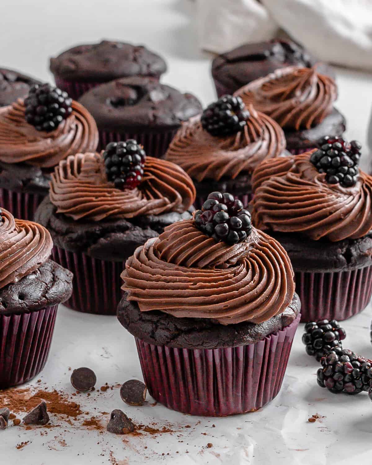 completed Blackberry Chocolate Cupcakes with blackberries scattered against a white surface