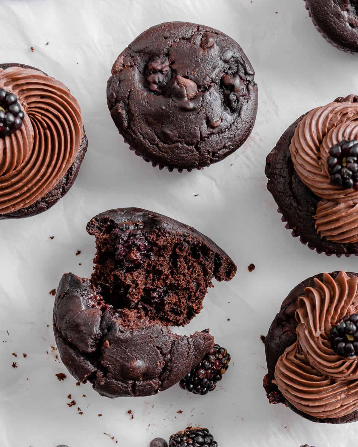 completed Blackberry Chocolate Cupcakes with one crumbled into two halves against a white surface