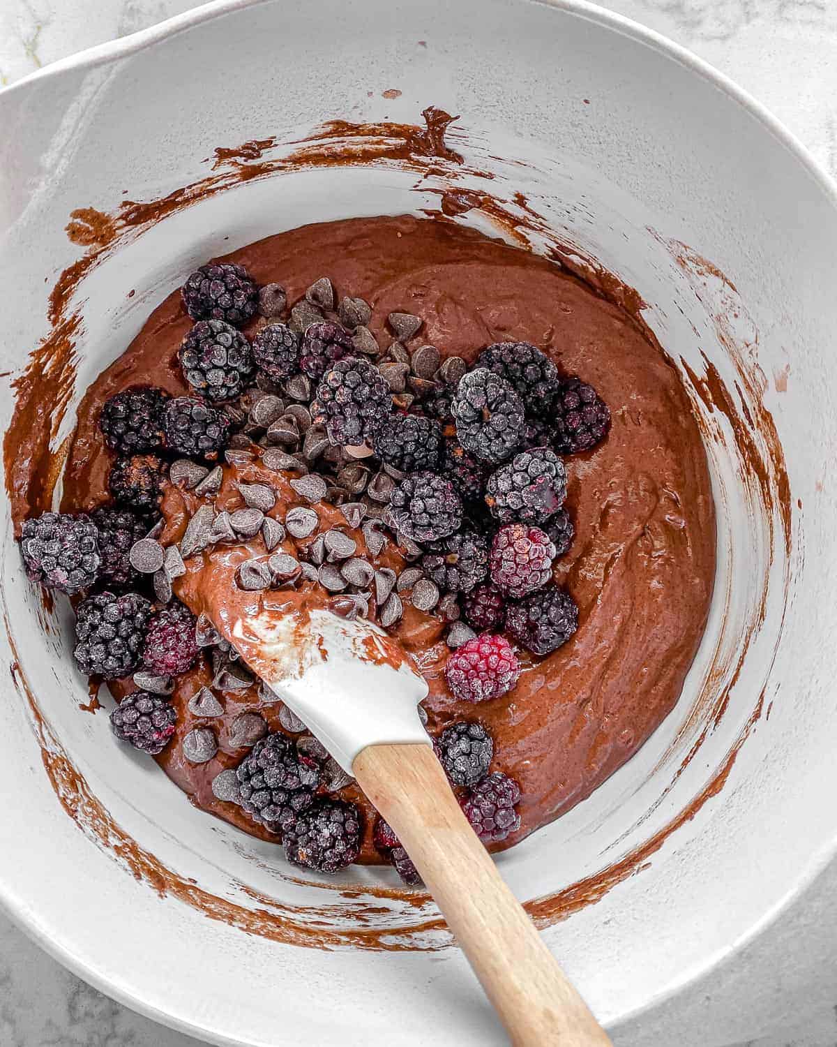 the addition of blackberries and chocolate chips added into Blackberry Chocolate Cupcakes batter in white bowl