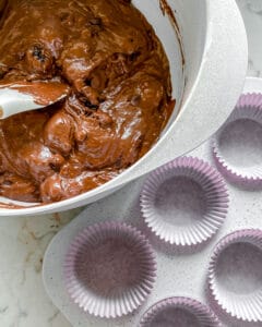process of mixing Blackberry Chocolate Cupcakes batter in white bowl with muffin tin in the background