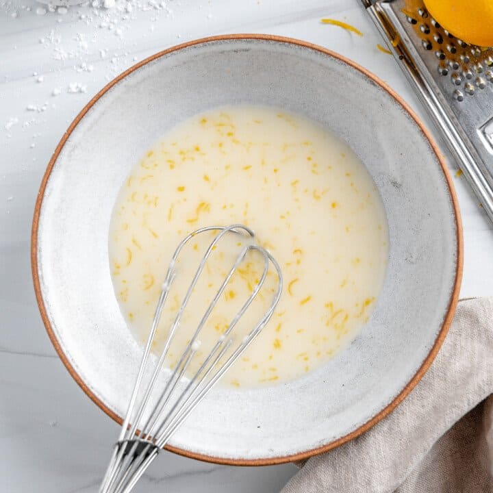 completed lemon glaze in white bowl with whisk in bowl against white background
