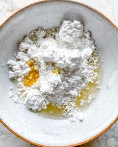 process of adding sugar to wet ingredients for lemon glaze in white bowl