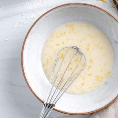 completed lemon glaze in white bowl with whisk in bowl against white background