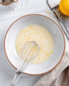 completed lemon glaze in white bowl with whisk in bowl against white background
