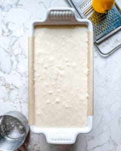 process of adding lemon loaf batter to tin against white background