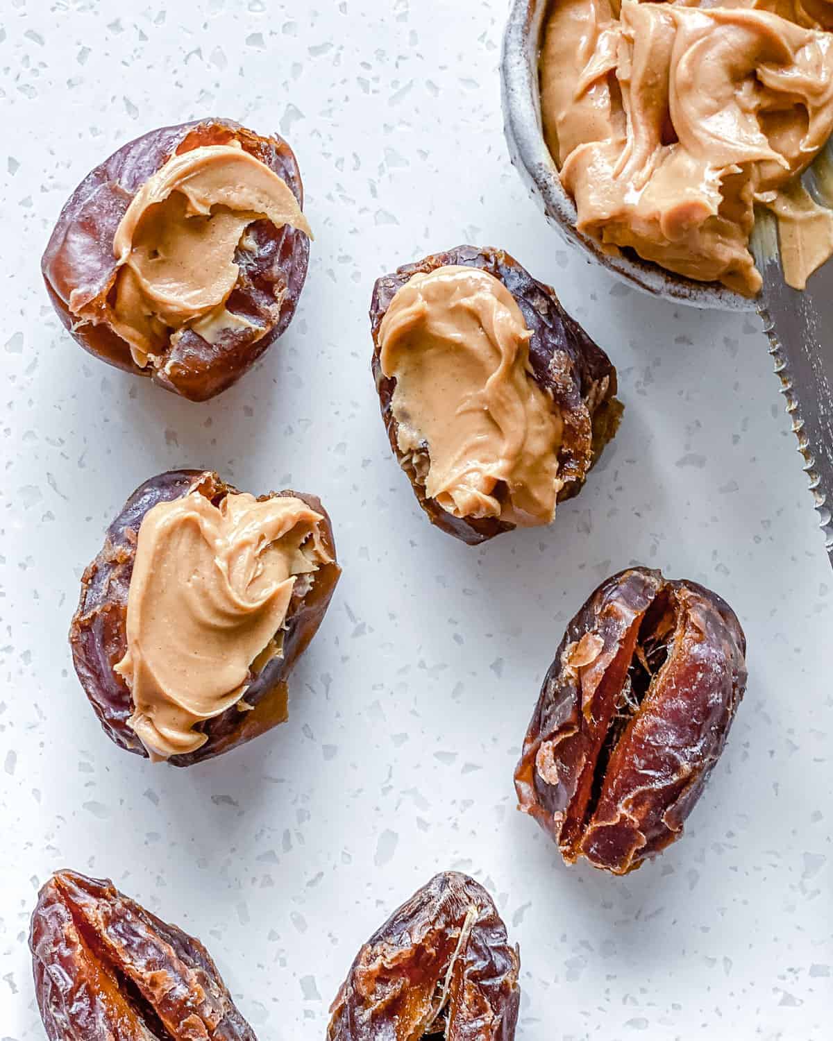 process of putting peanut butter in dates on white surface