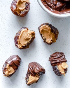 process of adding chocolate to peanut butter stuffed dates on white surface