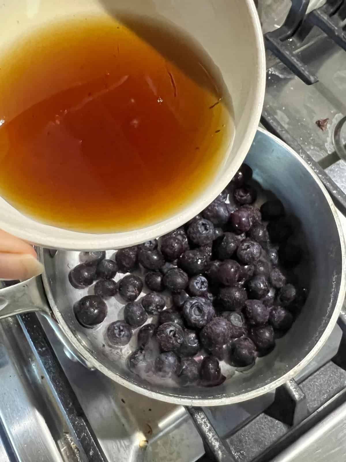 process of adding syrup to bowl of blueberries in a pot