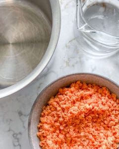 red lentils, water, and a saucepan placed on a white surface