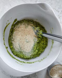 process of post adding bread crumbs and dried basil to Red Lentil Meatballs mixture in white bowl