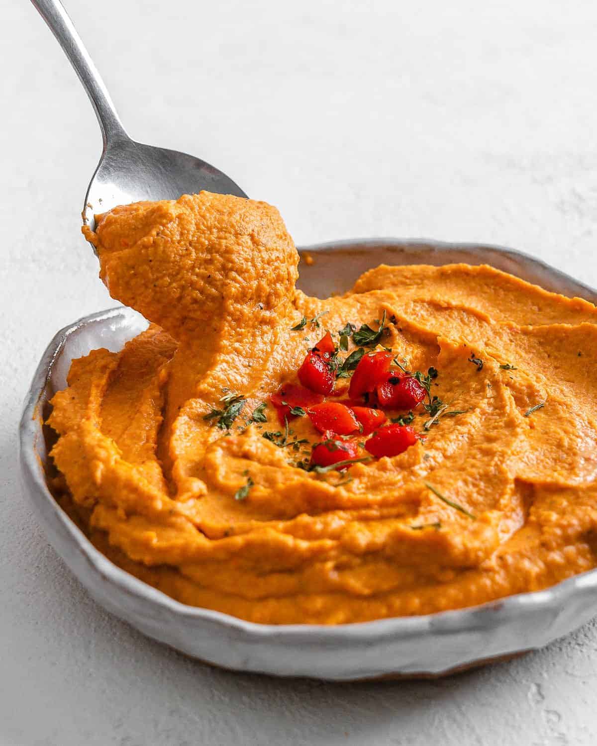 completed Smoky Roasted Red Pepper Hummus against a white background with a spoonful shown