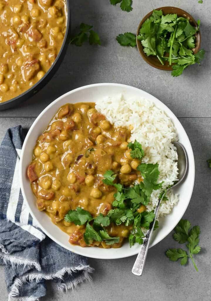 completed chickpea curry on a gray background with ingredients in the background