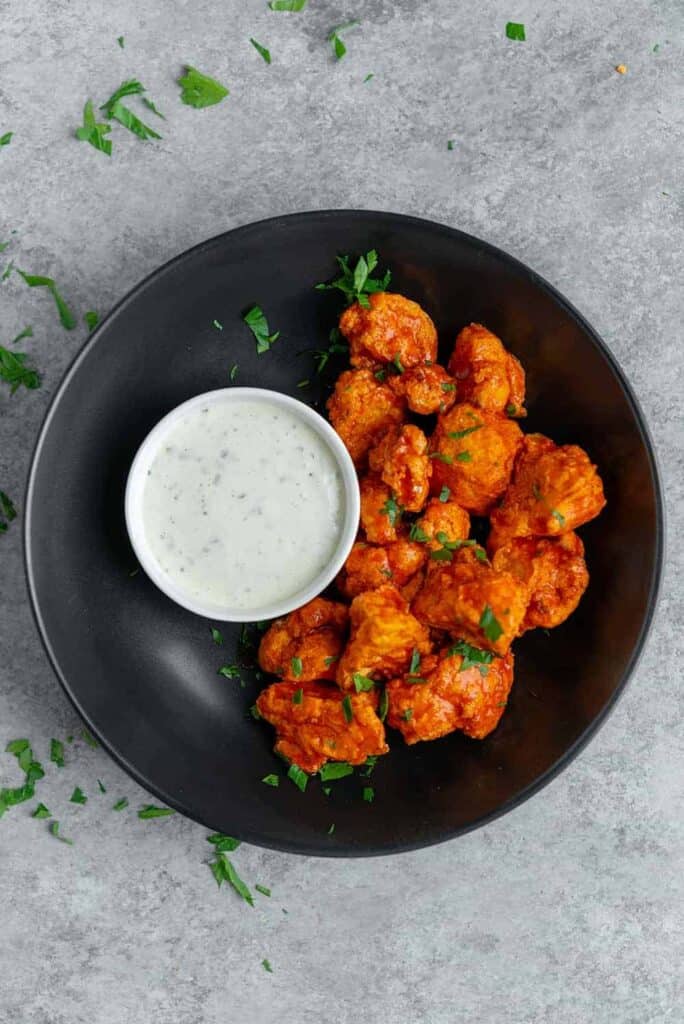 completed Air Fryer Buffalo Cauliflower Wings plated on a black plate against a gray background