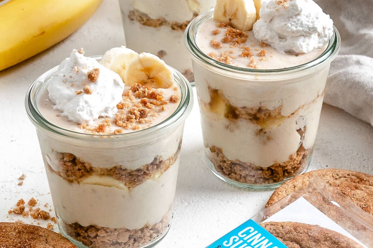 several completed banana parfait in glass jars with a cookie in the forefront