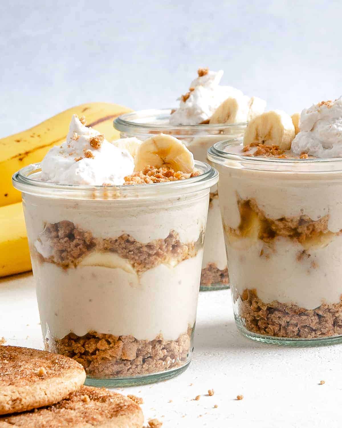 several completed banana parfait in glass jars against a white background