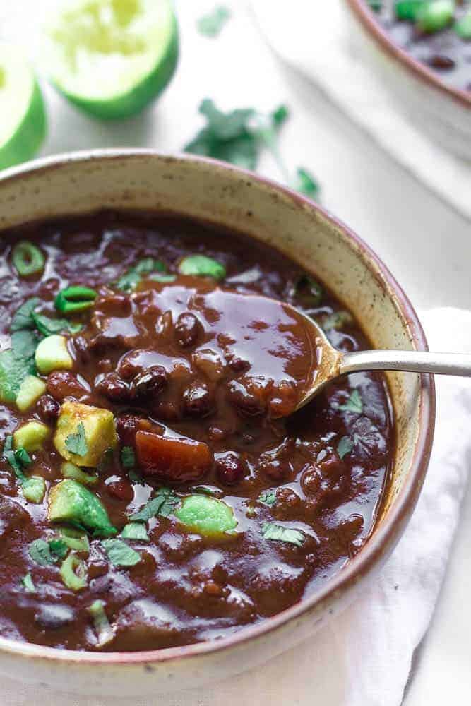 completed black bean soup in a light gray bowl against a white surface with ingredients scattered in the background