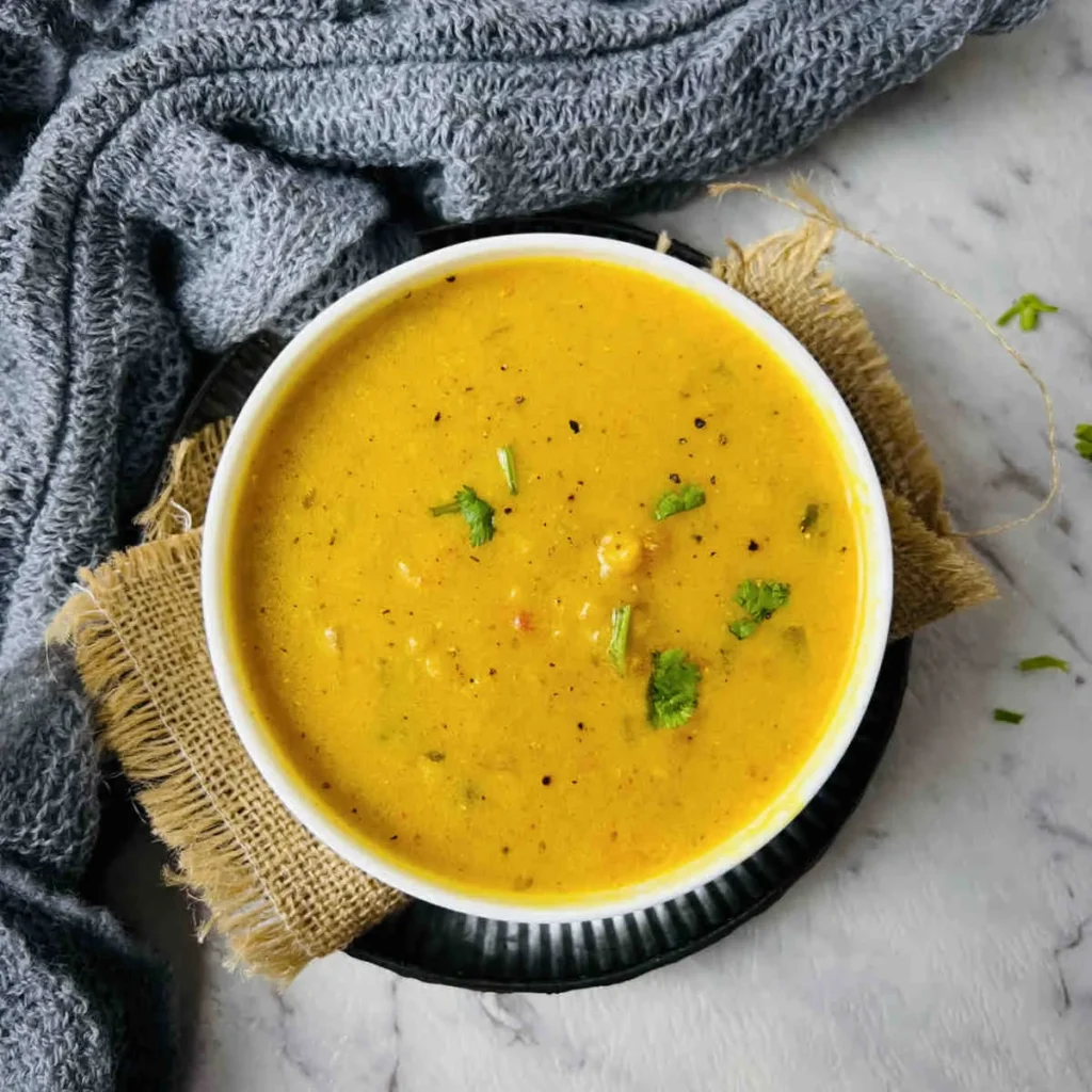 completed Mulligatawny Soup in a white bowl against a gray surface with a blue towel in the background