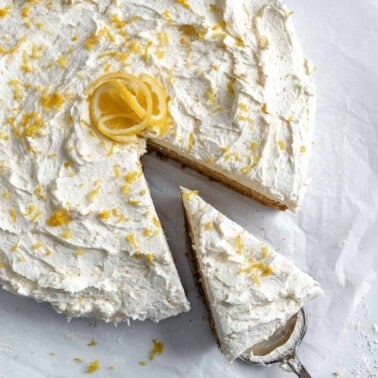 completed lemon frosting cake with a piece sliced out on a cake slicer utensil against a white background