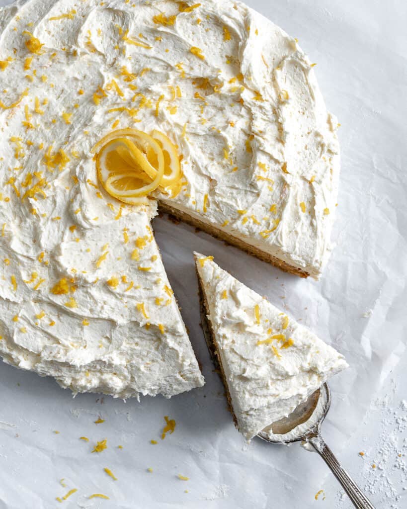 completed lemon frosting cake with a piece sliced out on a cake slicer utensil against a white background