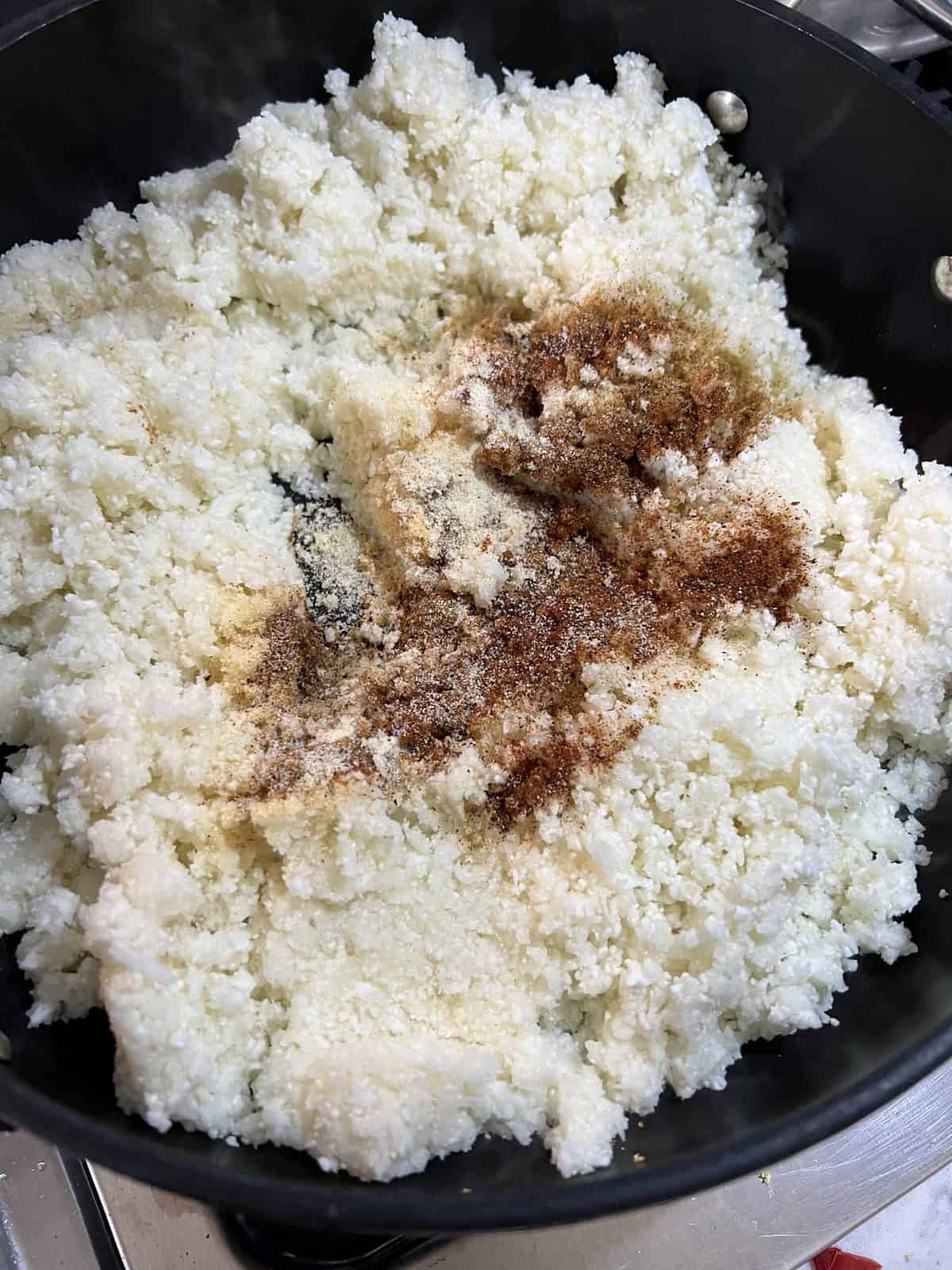 the addition of seasonings into riced cauliflower in a black pan