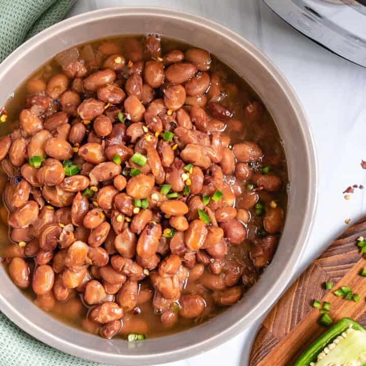 completed pinto beans in a bowl against a white counter with a light green cloth and brown cutting board in the background