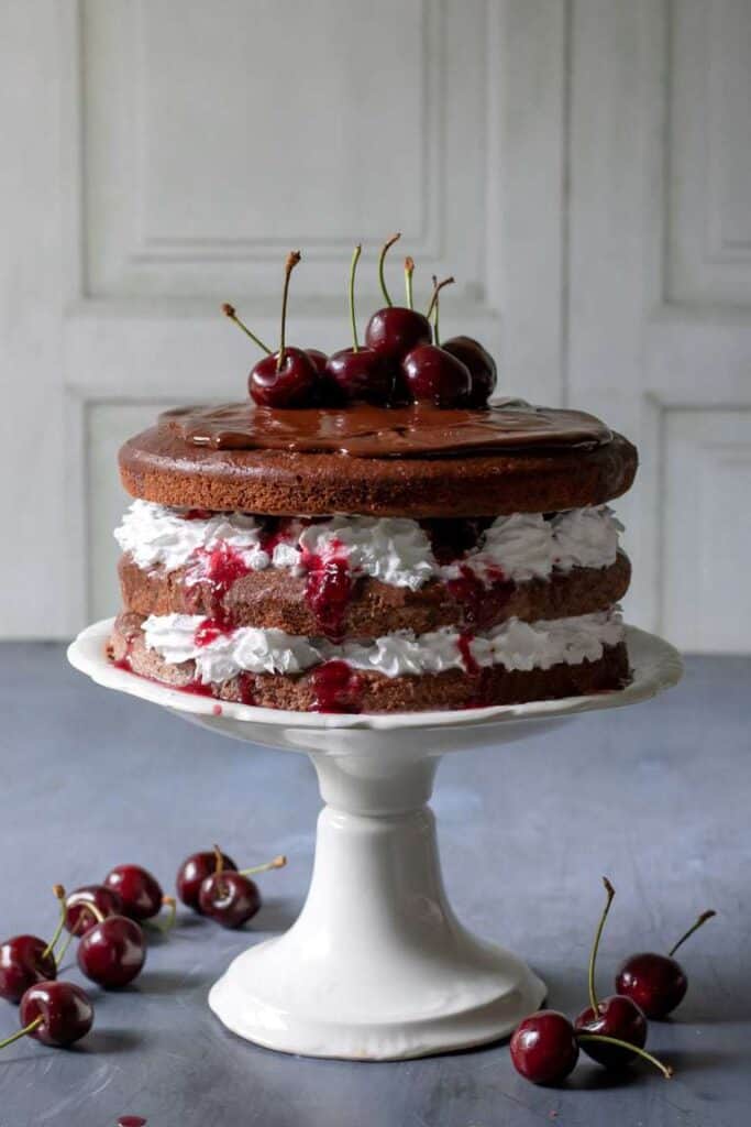 completed black forest cake on a cake platter against a gray table and white background