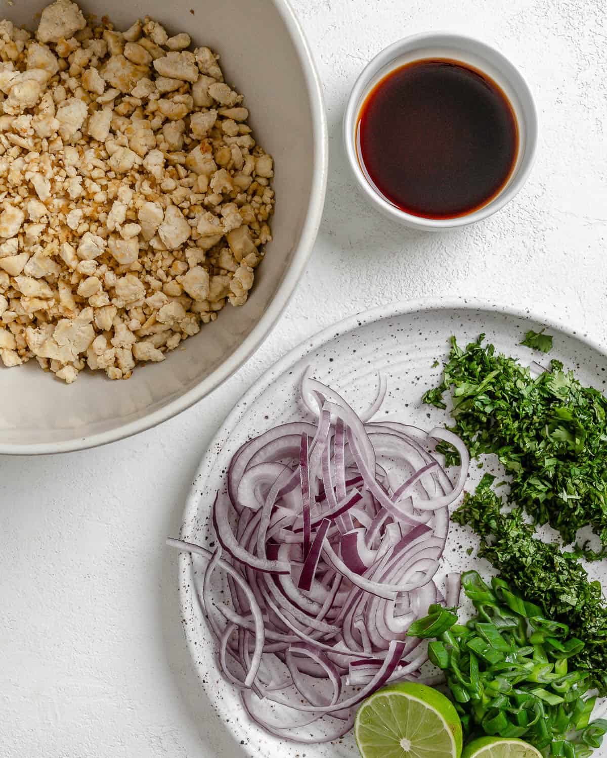 larb and veggies in two separate white bowls along side sauce against a white background
