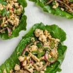 three completed larb salad servings against a white surface