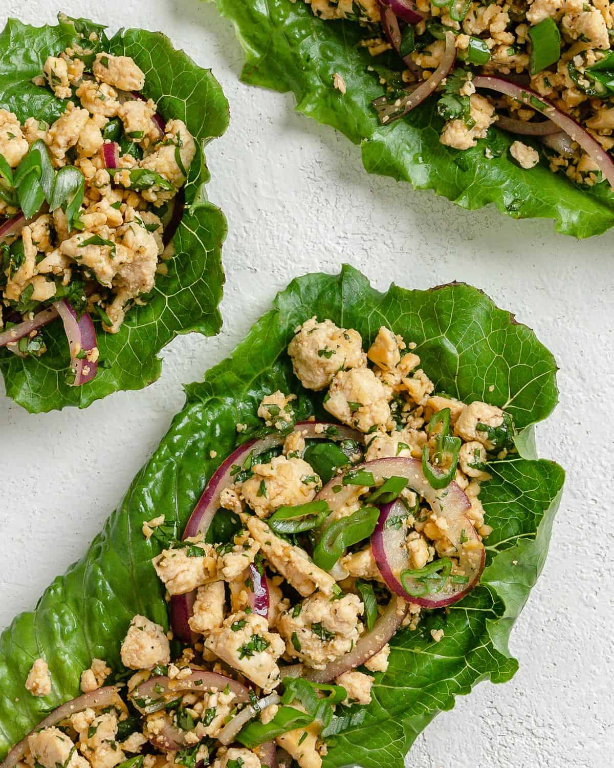 three completed larb salad servings against a white surface