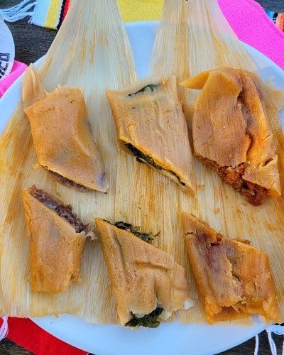completed vegan tamales halved on corn husk on a white plate