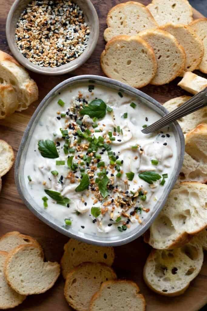 completed Caramelized Onion Dip in a gray bowl with bread  scattered in the background