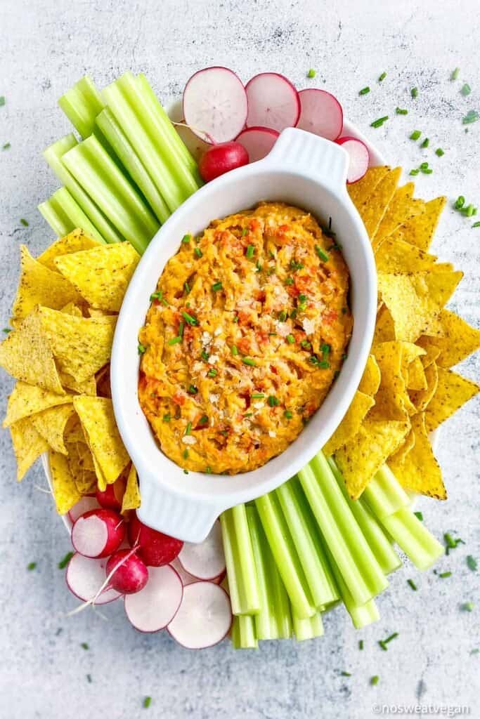 completed buffalo chickpea dip in white platter surrounded with chips and veggies against a white background