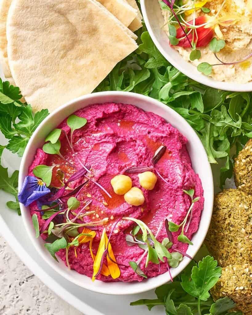 completed Pink Beetroot Hummus in a white bowl surrounded by greens and bread