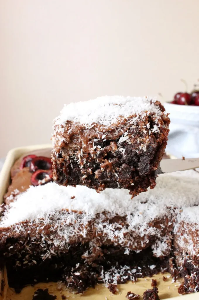 completed Vegan Chocolate Sheet Cake piece lifted above cake against a light background