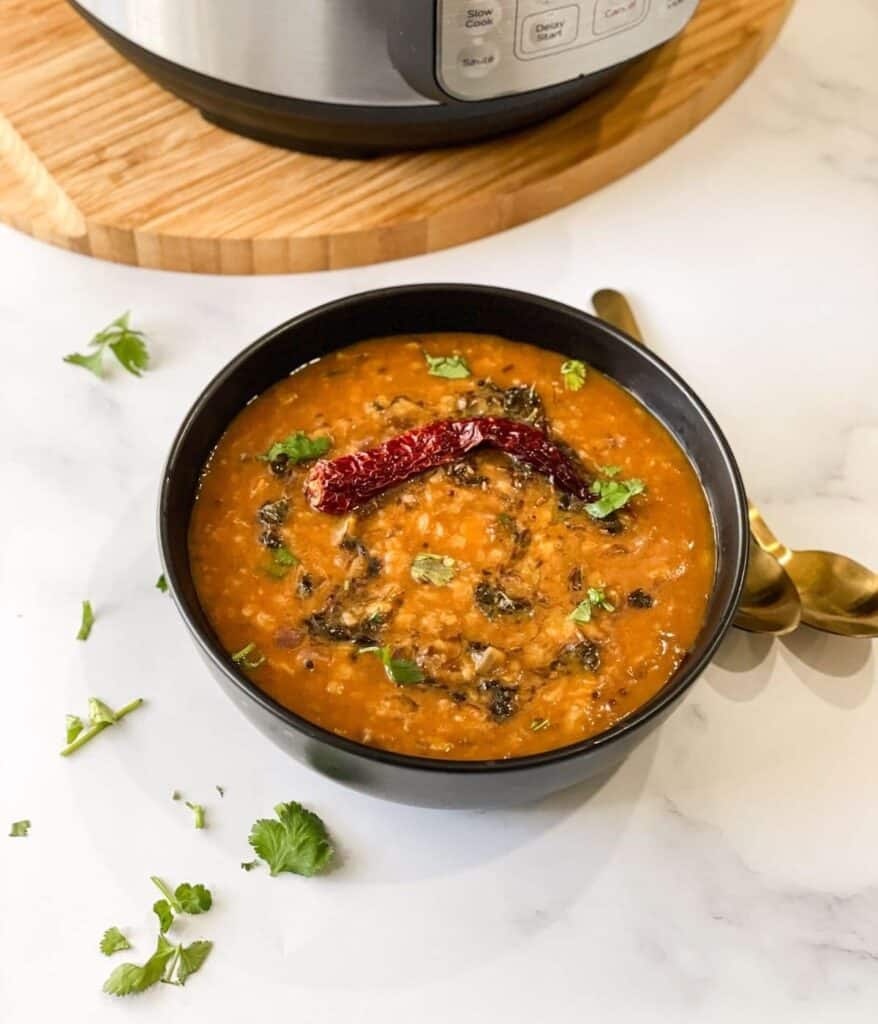 completed Dal Tadka Instant Pot Recipe in a small black bowl against a white background with herbs scattered against the surface