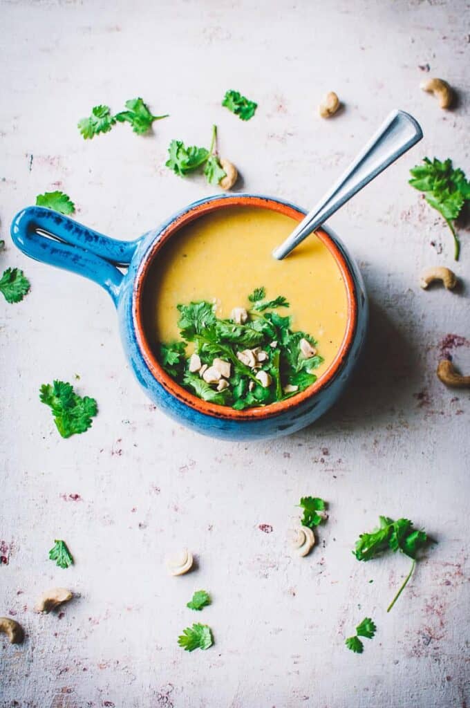 completed vegan cashew soup in a blue pot against a light background with scattered herbs