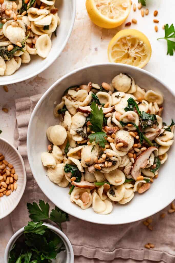 completed mushroom pasta in a white bowl with various ingredients in the background