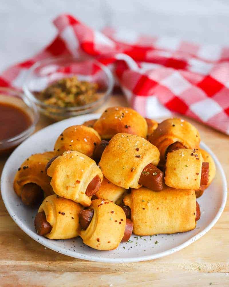 several completed Vegan Pigs in a Blanket on a white plate with a red and white towel in the background