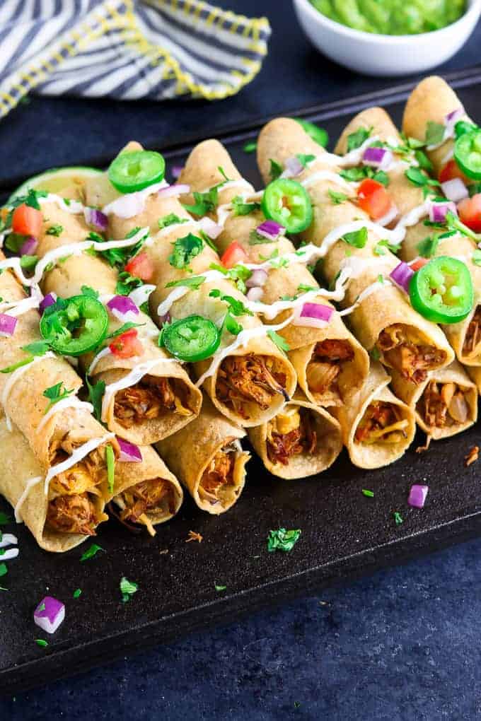 completed Vegan Baked Taquitos on a black surface dressed with veggies and sauce
