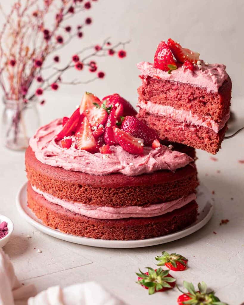 completed Vegan Strawberry Cake with a piece elevated against a white surface