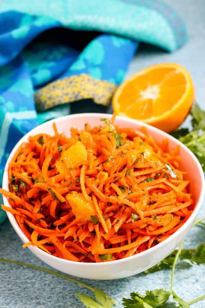 completed carrot salad in a white bowl with a half orange in the background