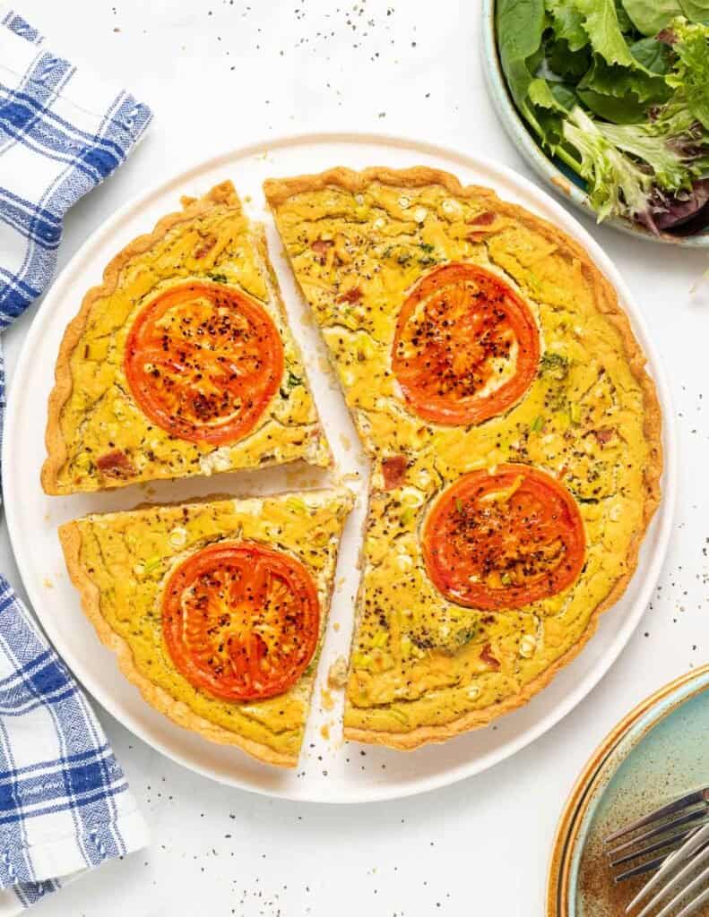 completed vegan quiche on a white plate with two slices cut from circular quiche 