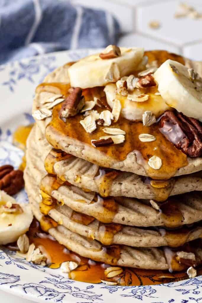 completed oat pancakes stacked on one another with syrup drizzling on the sides