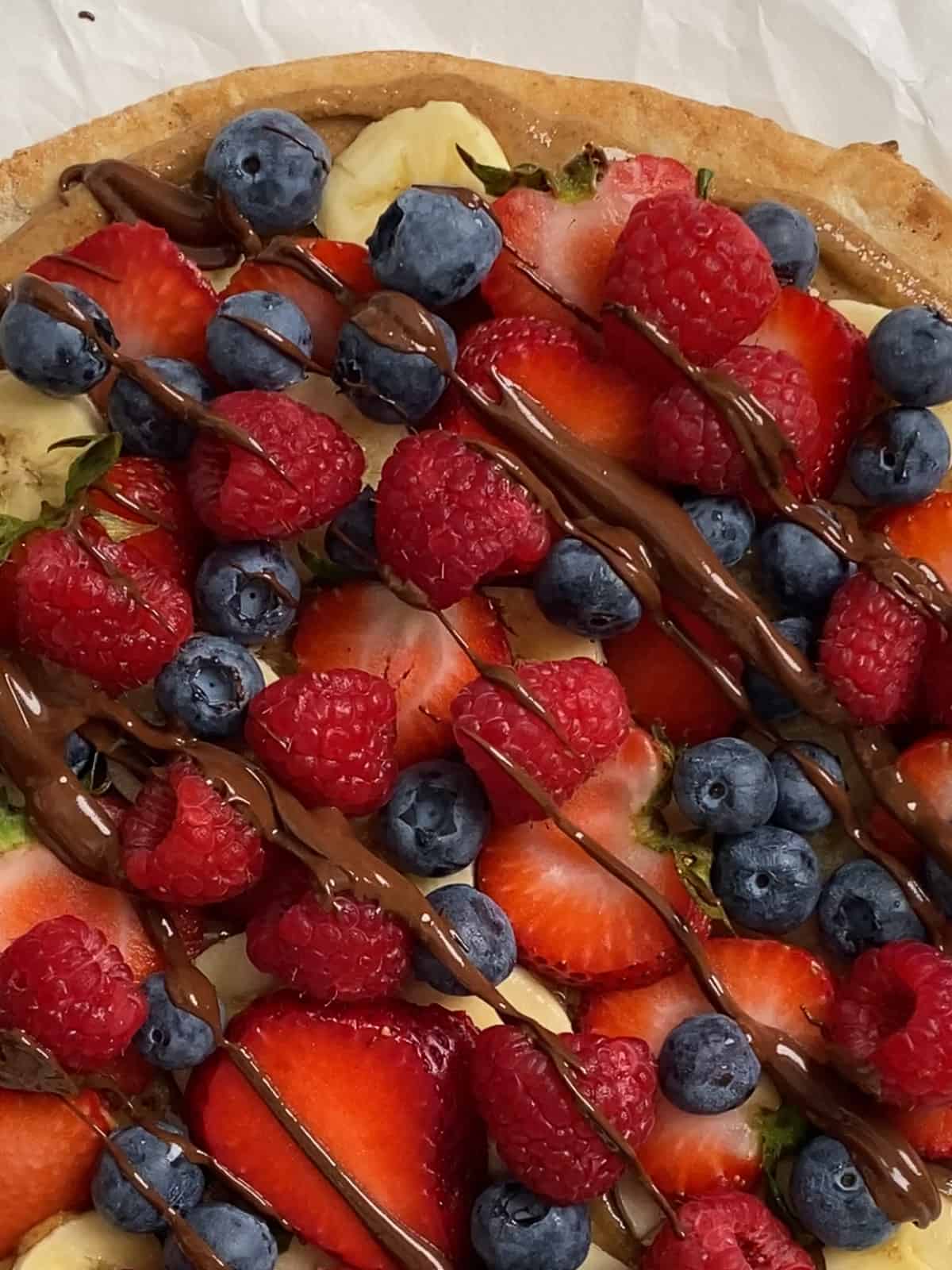 process of adding vegan chocolate drizzle to fruit pizza